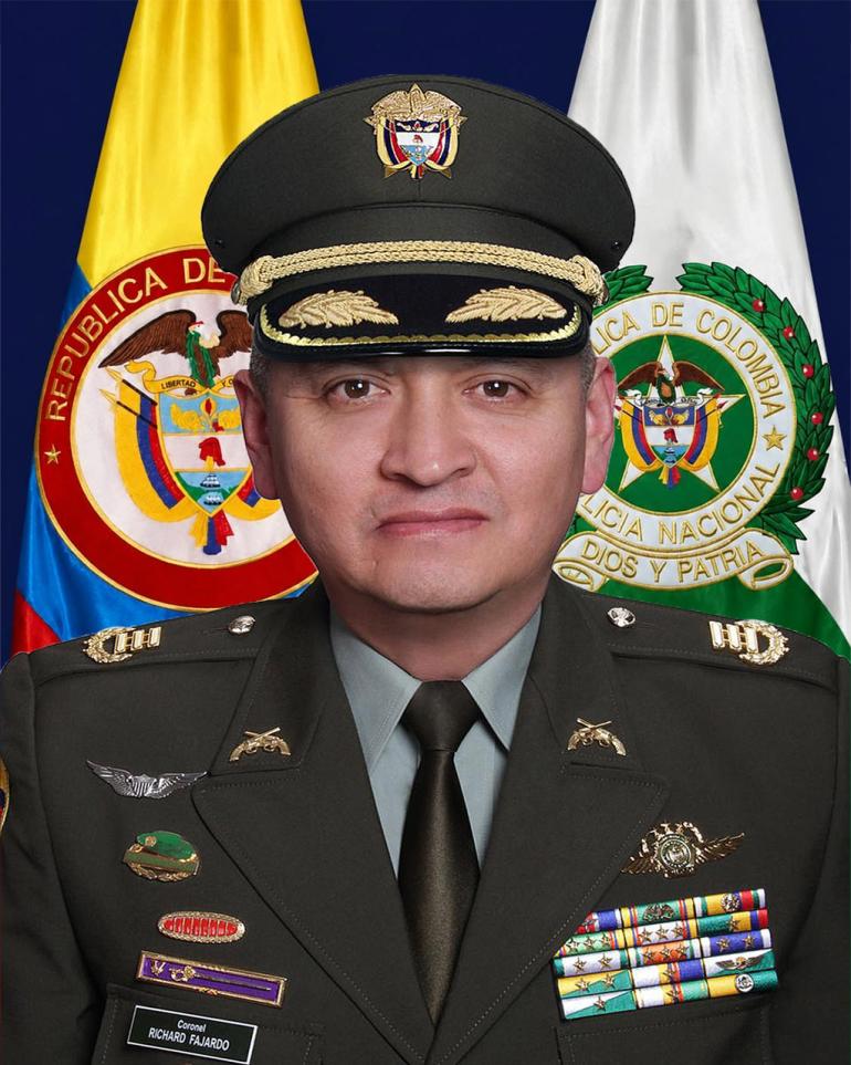Retrato oficial de una persona con uniforme de la Policía Nacional de Colombia, ubicado frente a las banderas de Colombia y de la institución; el uniforme incluye insignias, condecoraciones y una gorra de gala, coronel Richard Raúl Fajardo Ayala