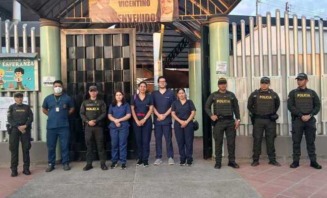 Auxiliares de policía y personal de salud frente a la fachada de una institución educativa