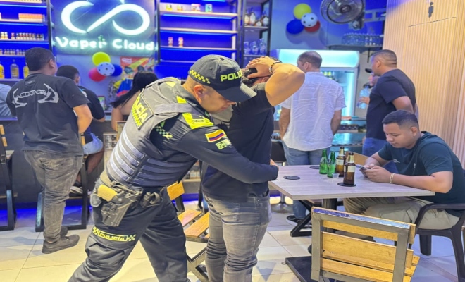 un uniformado de la policía  realizando un registro a persona en establecimiento abierto al publico 