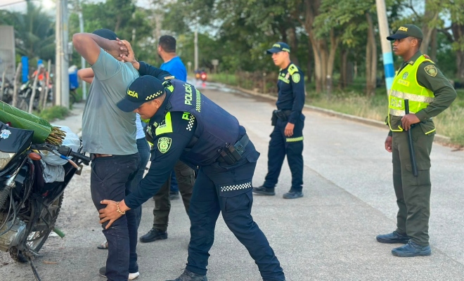 Grupo de funcionarios policiales, uno de ellos realizando registro a persona a un ciudadano.