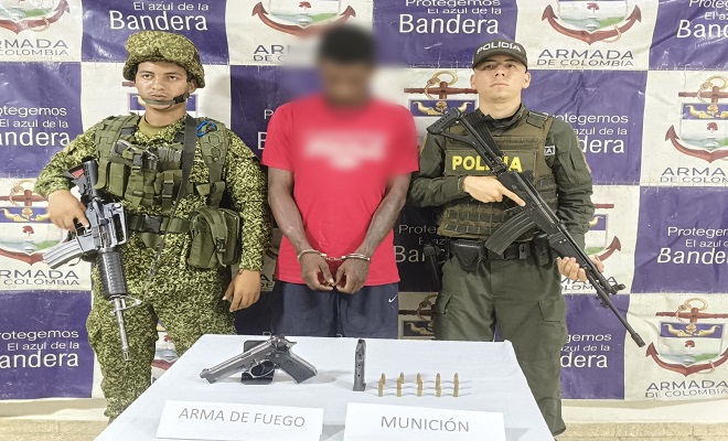 Un integrante de la Armada Nacional, una persona capturada y un uniformado de la Polic&iacute;a Nacional posan junto a una mesa donde se observa un arma de fuego tipo pistola, un proveedor y varios cartuchos de munici&oacute;n incautados