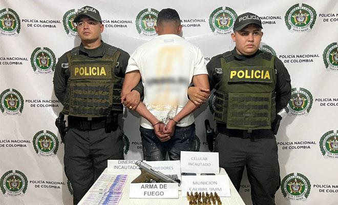 Dos uniformados, un capturado en el medio y encima de una mesa elementos incautados, arma de fuego, dinero, munición y un celular