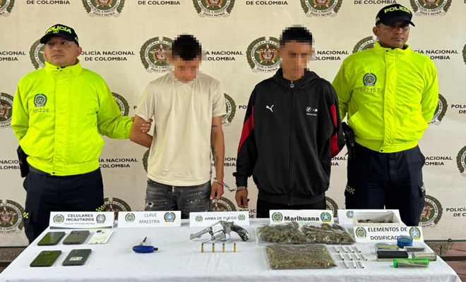 Se observa dos policía uniformados de la SIJIN con dos personas capturadas varios gramos de marihuana cinco celulares un revolver sobre y cuatro cartuchos sobre una mesa