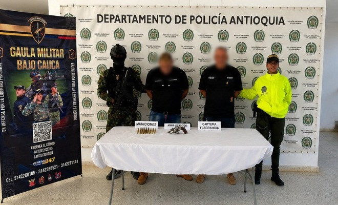 Un Policía y un soldado del Ejército custodian capturados y armamento