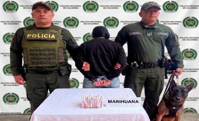 Dos funcionarios policiales con una ciudadana capturada frente a pendón institucional junto al canino Dimitrio con material incautado sobre mesa