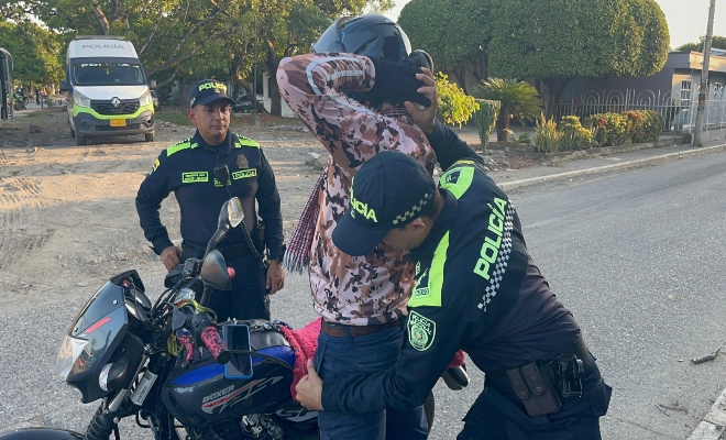 Dos funcionarios policiales realizando registro a persona a un ciudadano al lado de una motocicleta 
