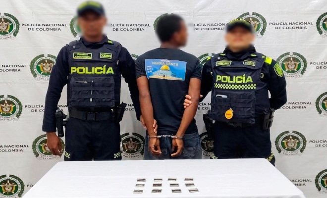Dos funcionarios policiales junto a un ciudadano capturado frente a pend&oacute;n institucional frente a ellos una mesa sobre la cual esta material incautado