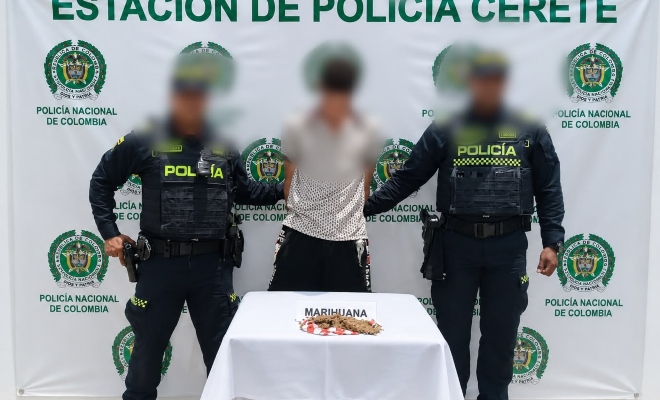 Dos funcionarios policiales con un ciudadano capturado frente a pend&oacute;n institucional frente a una mesa sobre la cual esta el material incautado 