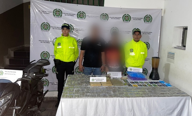 Dos polic&iacute;as custodiando dos capturados, una moto y estupefacientes
