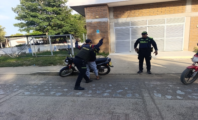 un policia registrando a un ciudadano y un policia prestando seguridad 