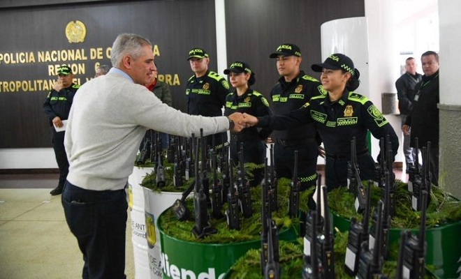 Gobernador del Departamento de Antioquia saludando a una funcionaria de la Policía Nacional, acompañados de 4 miembros uniformados y dos no uniformados de la institución, recibiendo 20 radios de comunicación para fortalecer la seguridad ciudadana.