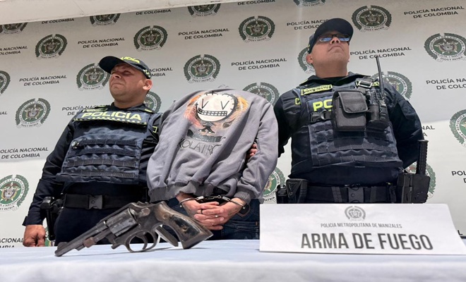 dos polic&iacute;as un capturado, arma de fuego incautada, mesa y un letrero 