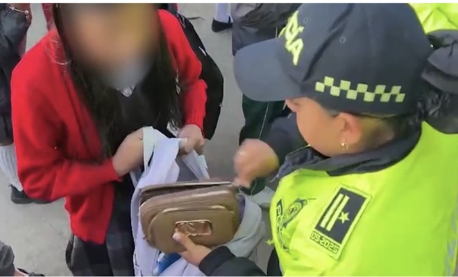 una polic&iacute;a haciendo un registro a un morral a un colegio 
