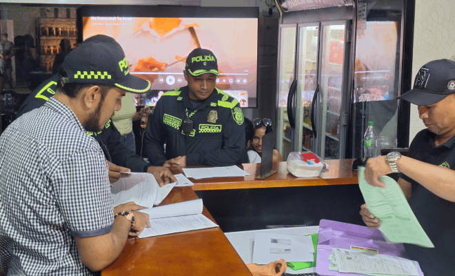 Dos policías observan un documento acompañados por un funcionario de la alcaldía mientras una persona con gorra y camisa negra sostiene un papel