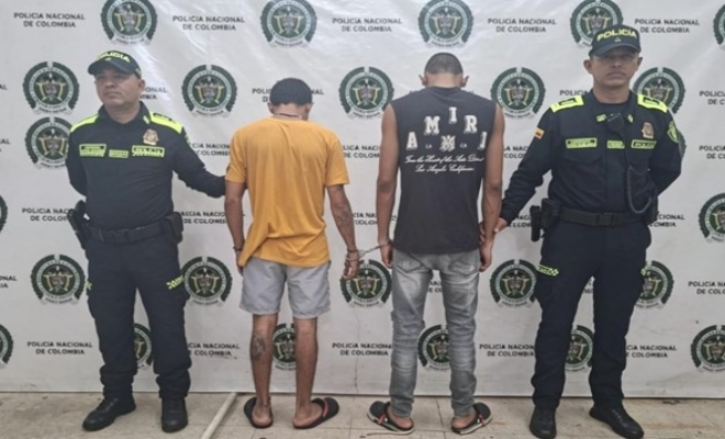dos policías custodian dos sujetos que están de espalda capturados por orden judicial 