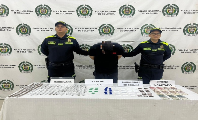 Dos uniformados con una persona capturada por el delito de tráfico, fabricación o porte de estupefacientes los cuales se muestran encima de una mesa