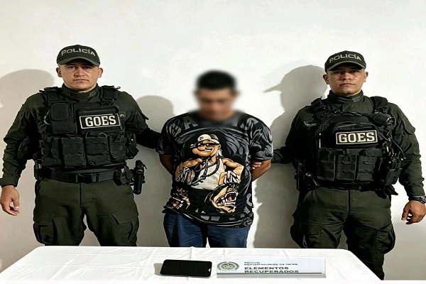 Dos policías custodian a un hombre capturado, junto al teléfono celular recuperado