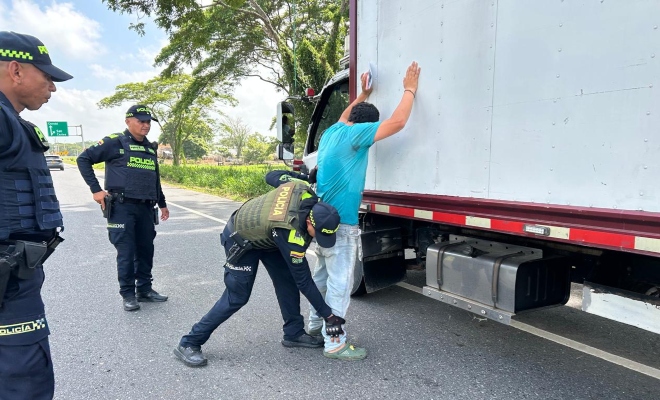 Tres funcionarios policiales realizando registro a persona a un ciudadano frente a un camión en la vía 