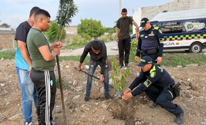 comunidad y tres uniformados organizando una cancha y siembra de árbol