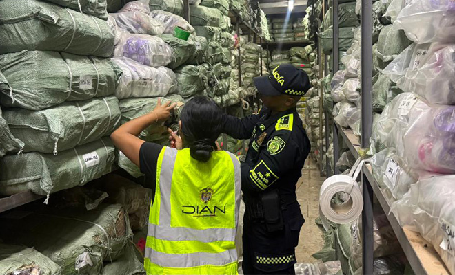 Un polic&iacute;a de la polic&iacute;a fiscal y aduanera y un funcionario de la dian inspeccionan mercanc&iacute;a ilegal hallada en varios paquetes