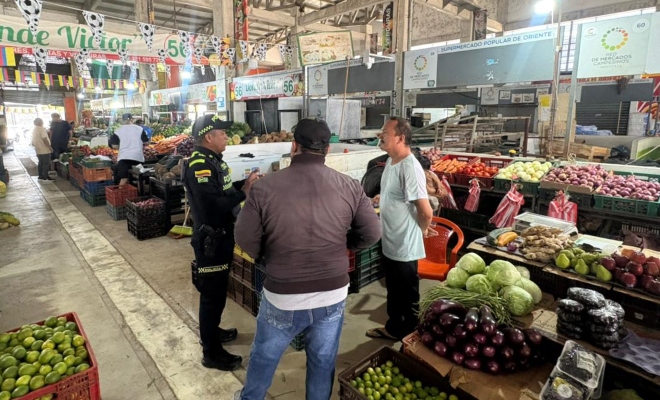 Funcionario de la Policía Nacional brindando recomendaciones a dos ciudadanos en plaza de mercado 