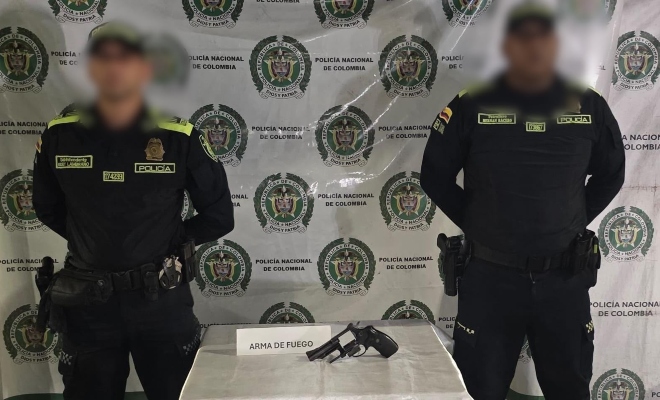 Dos funcionarios policiales frente a ellos una mesa con el arma de fuego hallada y de fondo el pendón institucional  