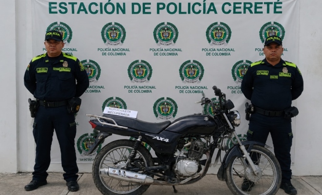dos funcionarios policiales frente al pendón institucional con una motocicleta recuperada