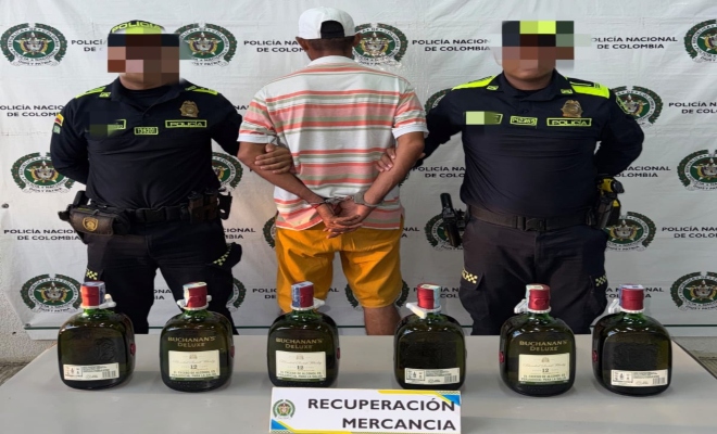 Dos funcionarios policiales con un ciudadano capturado frente a pendón institucional  y incautación de botellas de alcohol 
