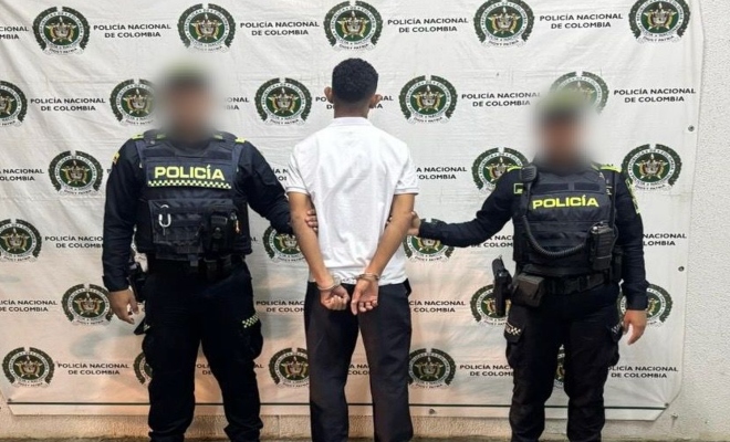 Dos funcionarios policiales con un ciudadano capturado frente a pendón institucional 