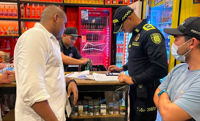 Funcionario policial realizando verificación de documentación de los establecimientos abiertos al publico junto a dos delegados de Administración Municipal y administrador del local