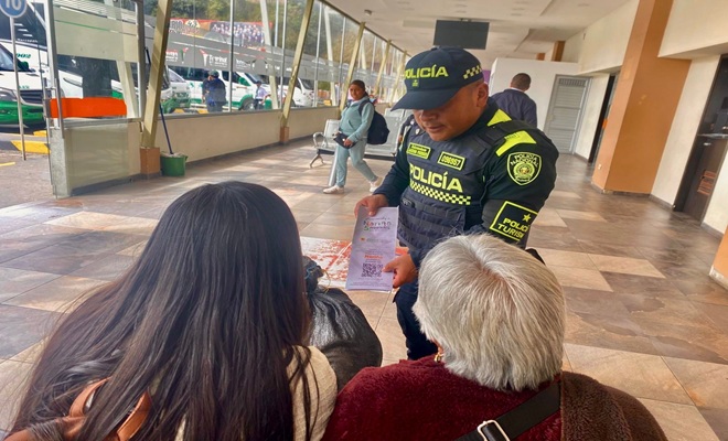 dos ciudadanas sentadas de espalda y un funcionario policial dando a conocer un cartel
