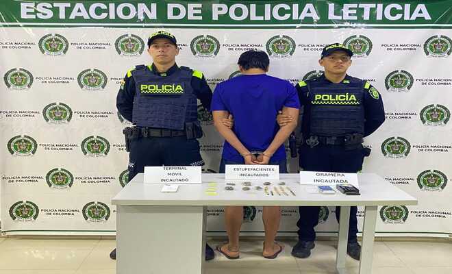 Dos polic&iacute;as, una persona capturada de espaldas y encima de una mesa elementos incautados