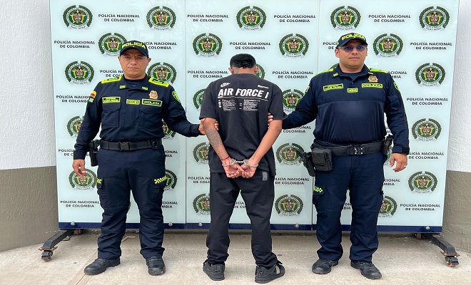 Una persona de espaldas capturada por el delito de concierto para delinquir y homicidio y dos Policías brindando seguridad