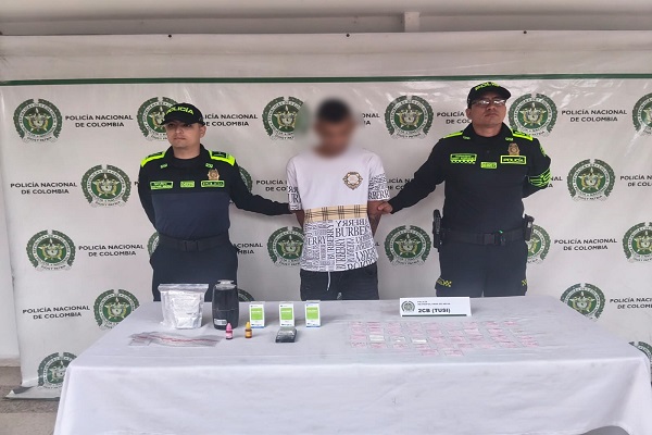 Dos Policías con un hombre capturado, por el delito de estupefacientes y encima de una mesa elementos incautados