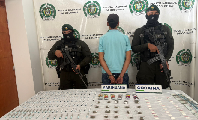 Hombre capturado en medio de dos policías, en frente elementos incautados