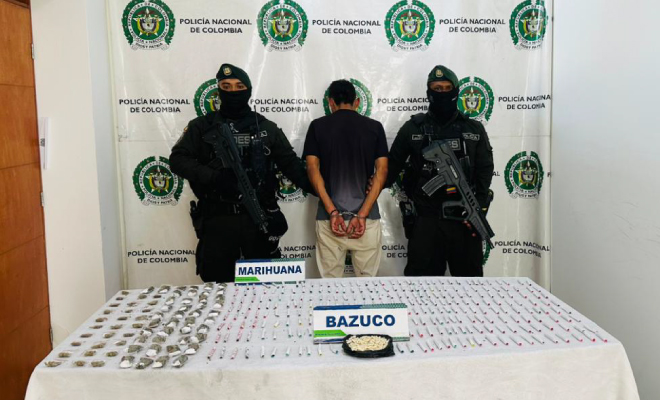 Hombre capturado en medio de dos policías, en frente estuperfacientes incautados