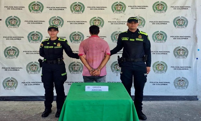 Un hombre de espaldas capturado por orden judicial por el delito de hurto y dos Polic&iacute;as brindando seguridad.