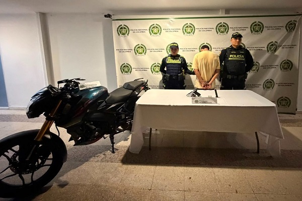 Dos policías custodian a un hombre capturado junto a una mesa con un arma traumática incautada y una motocicleta recuperada