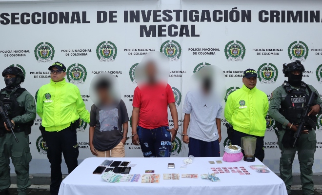 tres capturados y cuatro policias junto a mesa con incautaciones