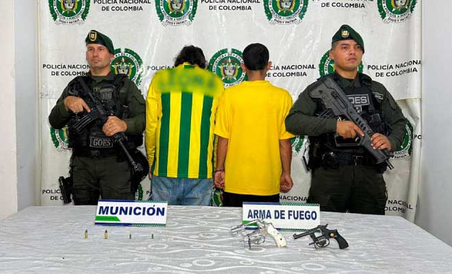 Dos hombres capturados en medio de dos Policías, en frente armas de fuego incautadas.