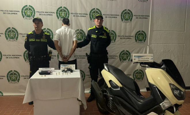 Hombre capturado en medio de dos policías, en frente elementos incautados