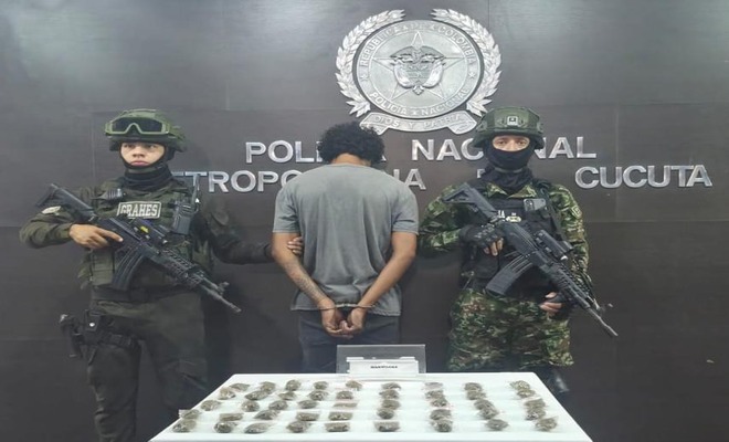 Persona esposada junto a uniformados de la Policía Nacional, con varios paquetes pequeños dispuestos sobre una mesa