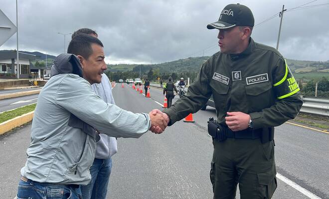 Un uniformado d ela Policía dando la mano a dos ciudadanos en la vía 