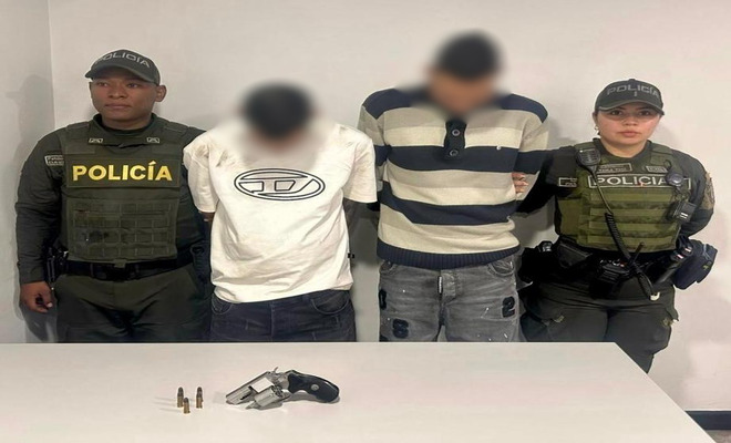 Dos policias con dos capturados y encima de una mesa un arma de fuego