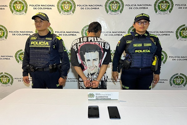 Dos uniformados presentan a una persona capturada junto a dos celulares recuperados encima de una mesa