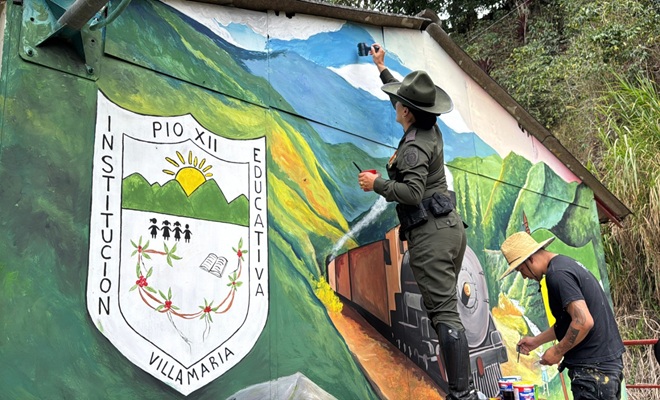 una mujer policía y un ciudadano pintando una pared una escuela de niños de la zona rural 
