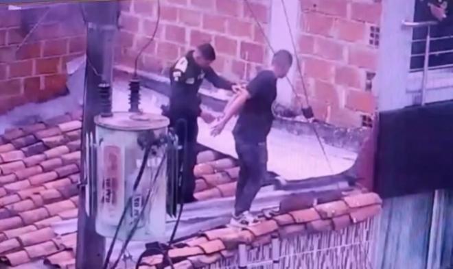 Un polic&iacute;a y una persona capturada sobre los techos de algunas viviendas. En la escena se observa un transformador el&eacute;ctrico y cables cercanos