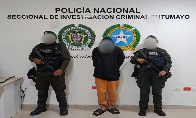 Dos policías presentan a capturado de frente hacia una pared con logos institucionales de la Policía Nacional