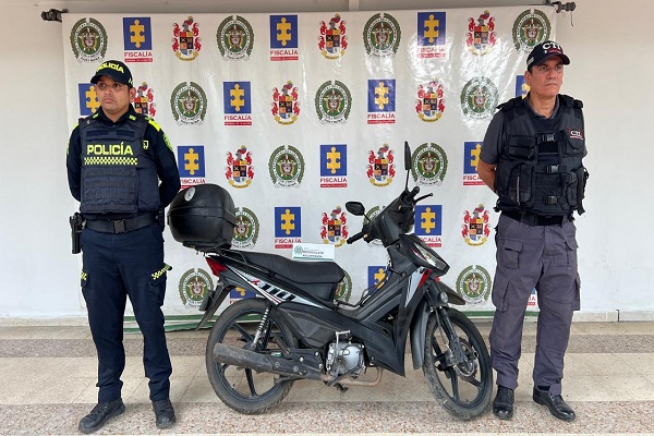 Un policía y un funcionario del CTI presentan una motocicleta recuperada durante un operativo de allanamiento