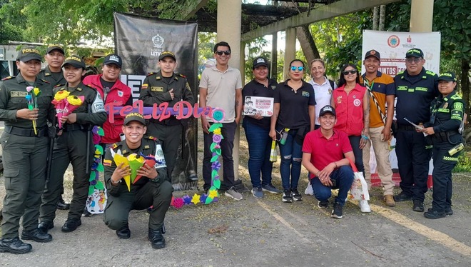 En la fotografía se observa a un grupo de policías, funcionarios y colaboradores reunidos en un espacio al aire libre durante una jornada comunitaria en el Amazonas. Varias personas sostienen flores y decoraciones coloridas alrededor de un letrero de “Feliz Día”, reflejando un ambiente de unión, reconocimiento y compañerismo. La imagen transmite el compromiso de las instituciones con la seguridad, la protección integral y el fortalecimiento de las relaciones con la comunidad y el turismo en la región 